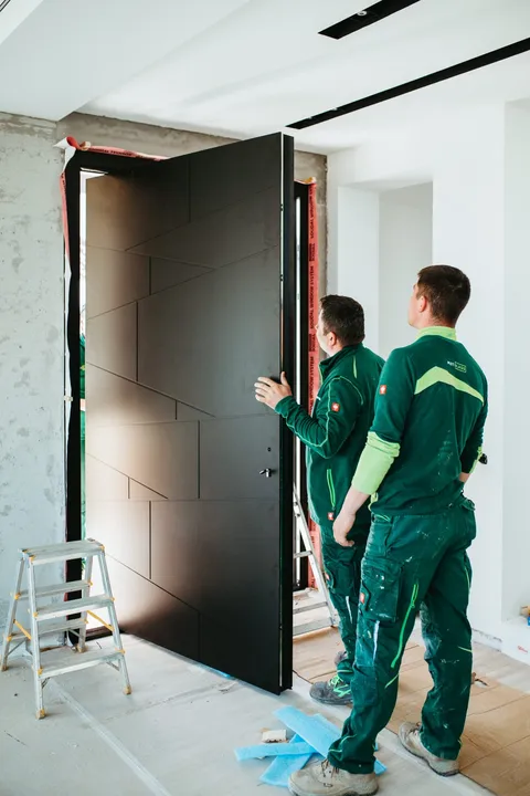 Ușa deschisă văzută din interior, cu desen geometric pe fața interioară și echipa lângă canat