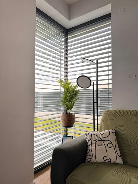 Colțul vitrat la 90° văzut din interior, cu jaluzeaua exterioară coborâtă pe ambele laturi