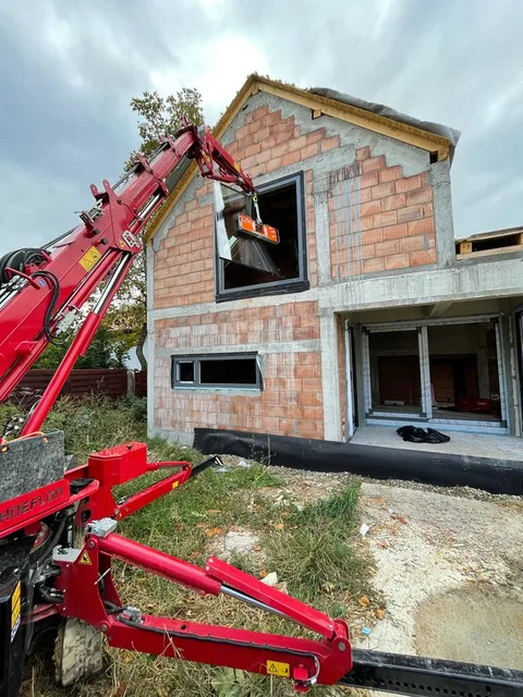 Mini-macara cu dispozitiv de prindere a sticlei în dreptul ferestrei de la etaj, în șantier