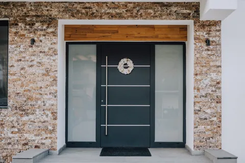 Ușa de intrare din aluminiu, antracit, cu panouri laterale mate, în ancadramentul din piatră
