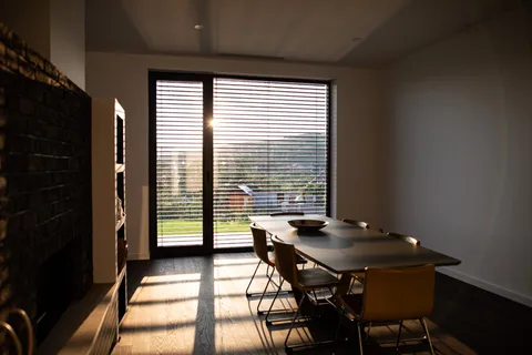 Zona de dining cu un vitraj înalt până la tavan și jaluzea exterioară