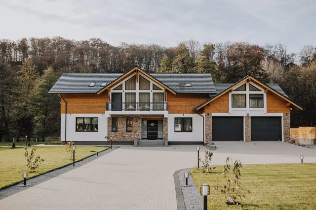 Casa din Sovata văzută din fața aleii de acces, cu fațada albă, placare din lemn și ferestre cu tâmplărie antracit la exterior